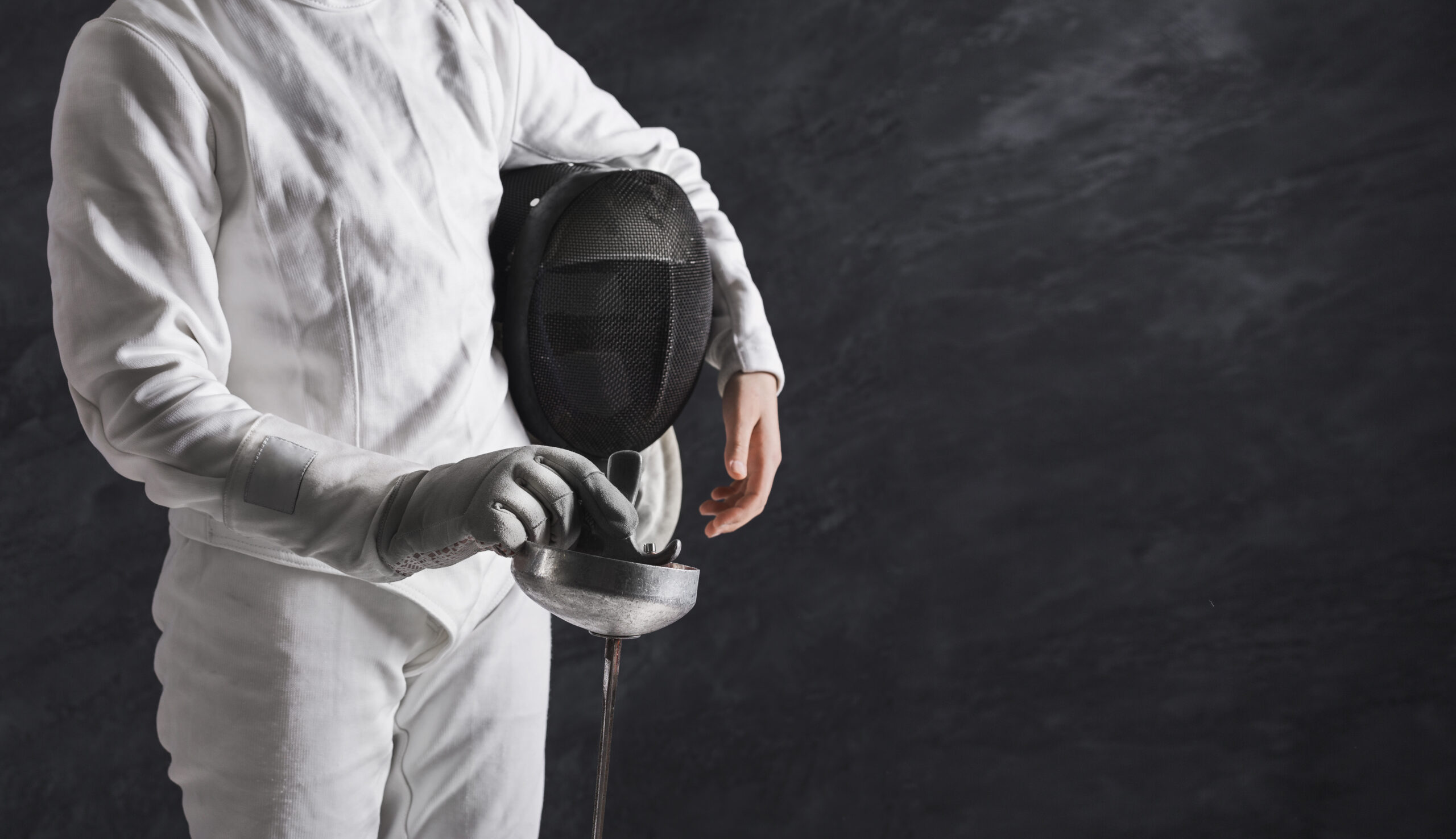 Female fencer in white fencing suit at black background